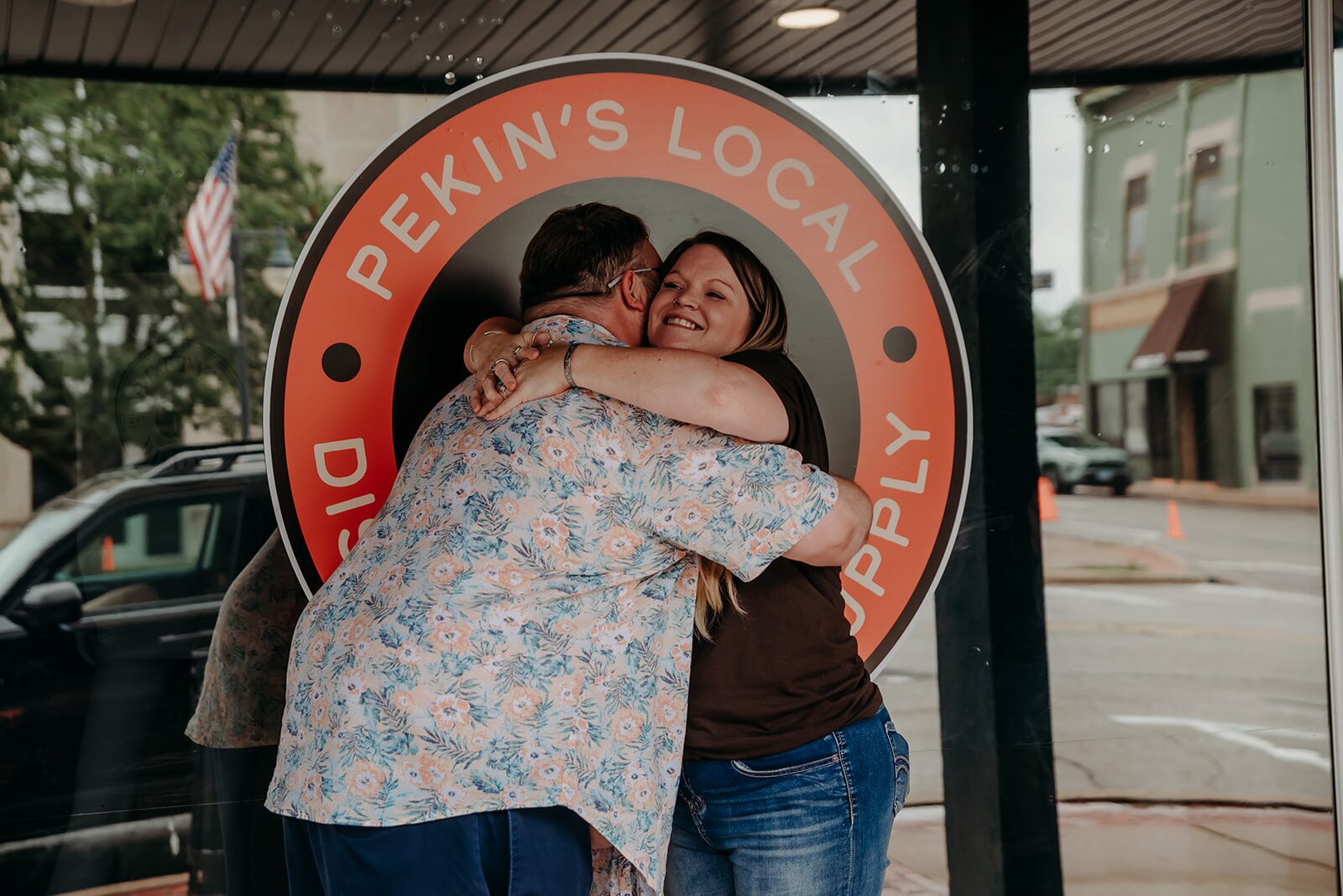 Two people embrace in front of the flame logo window at Pekin's Local Dispensary in downtown Pekin, IL